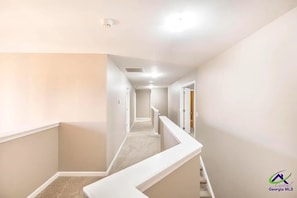 A narrow, carpeted hallway with white walls and a white railing.