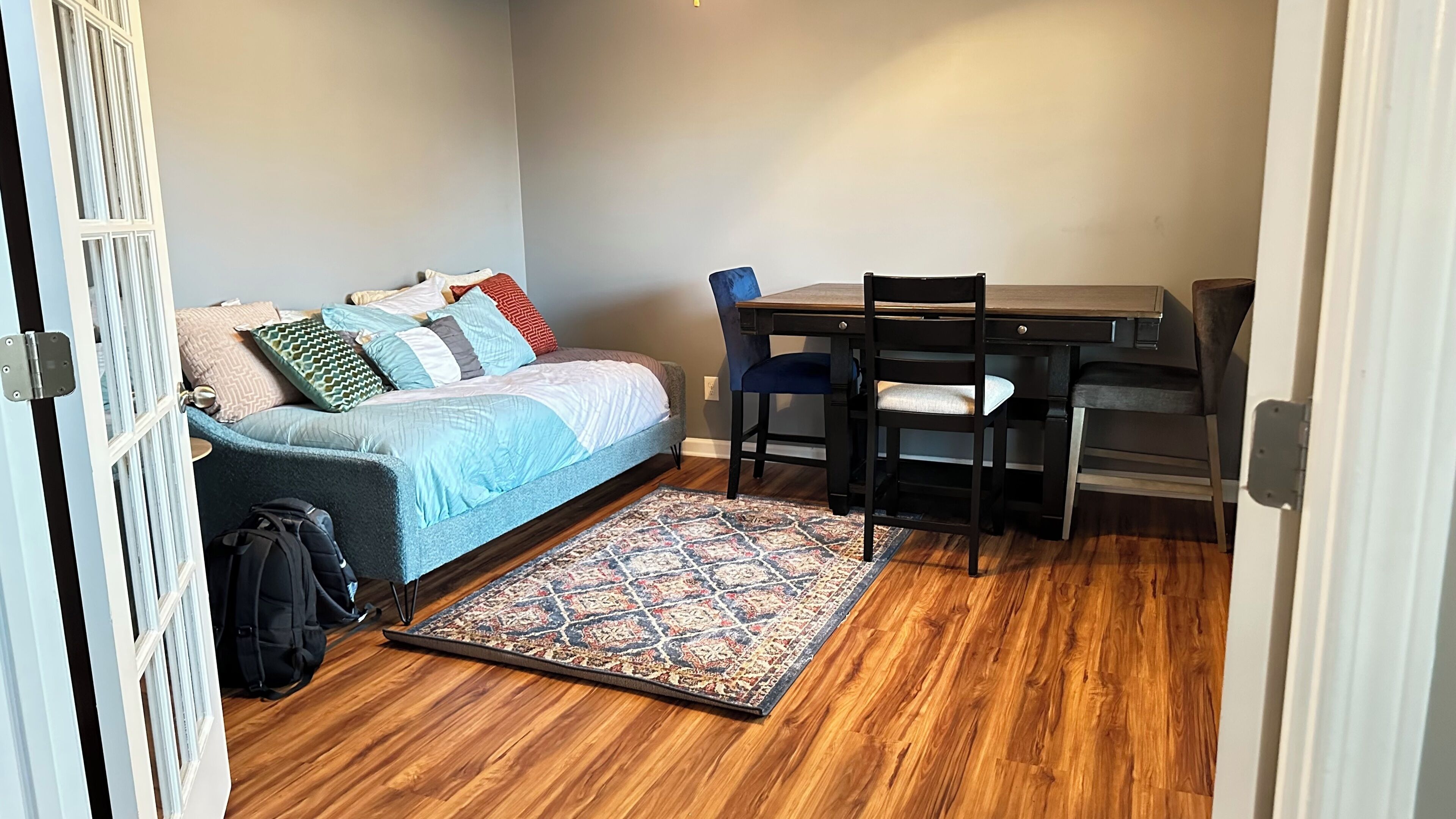 A compact room with a bed, a desk, a chair, and a patterned rug.