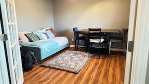 A compact room with a bed, a desk, a chair, and a patterned rug.