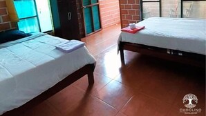 A room with two beds, a window with curtains, and a brick wall.