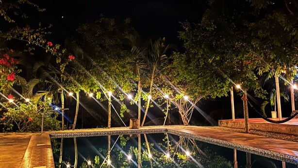 A nighttime pool area with a tiled deck, surrounded by trees and illuminated by string lights.