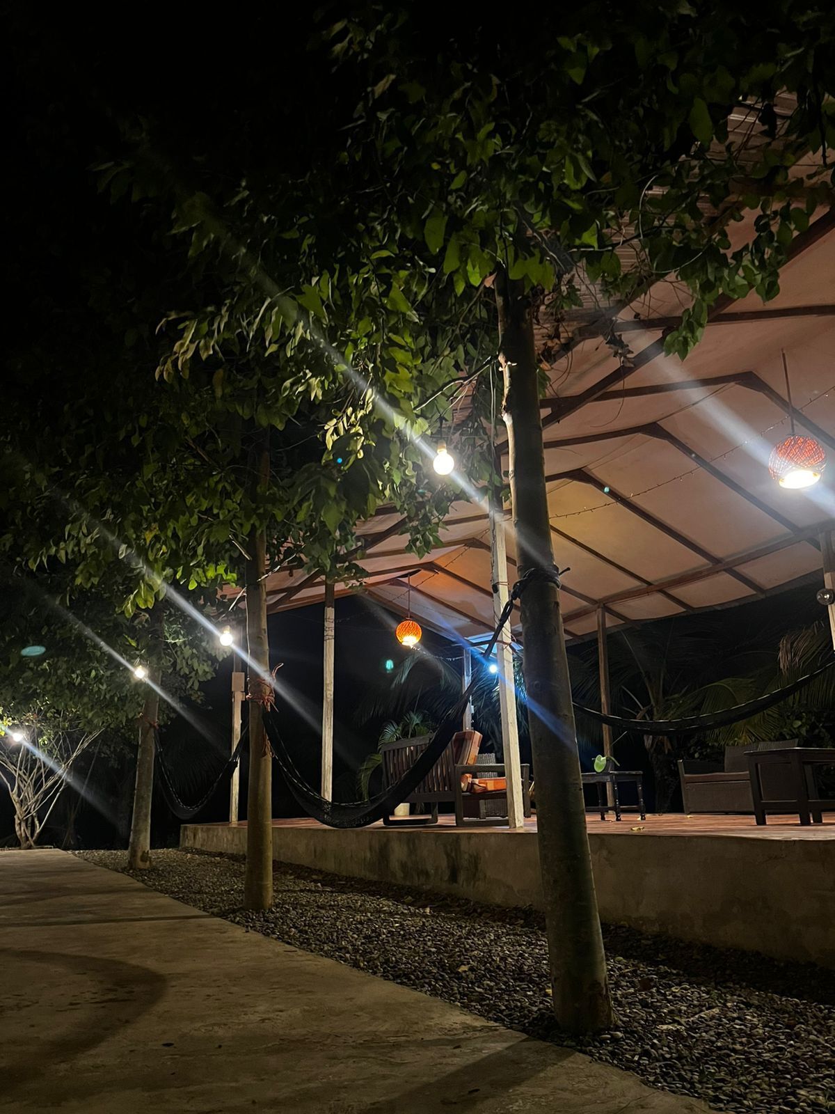 Un espace extérieur aménagé avec des hamacs, des tables et des chaises, le tout installé sous une structure couverte.