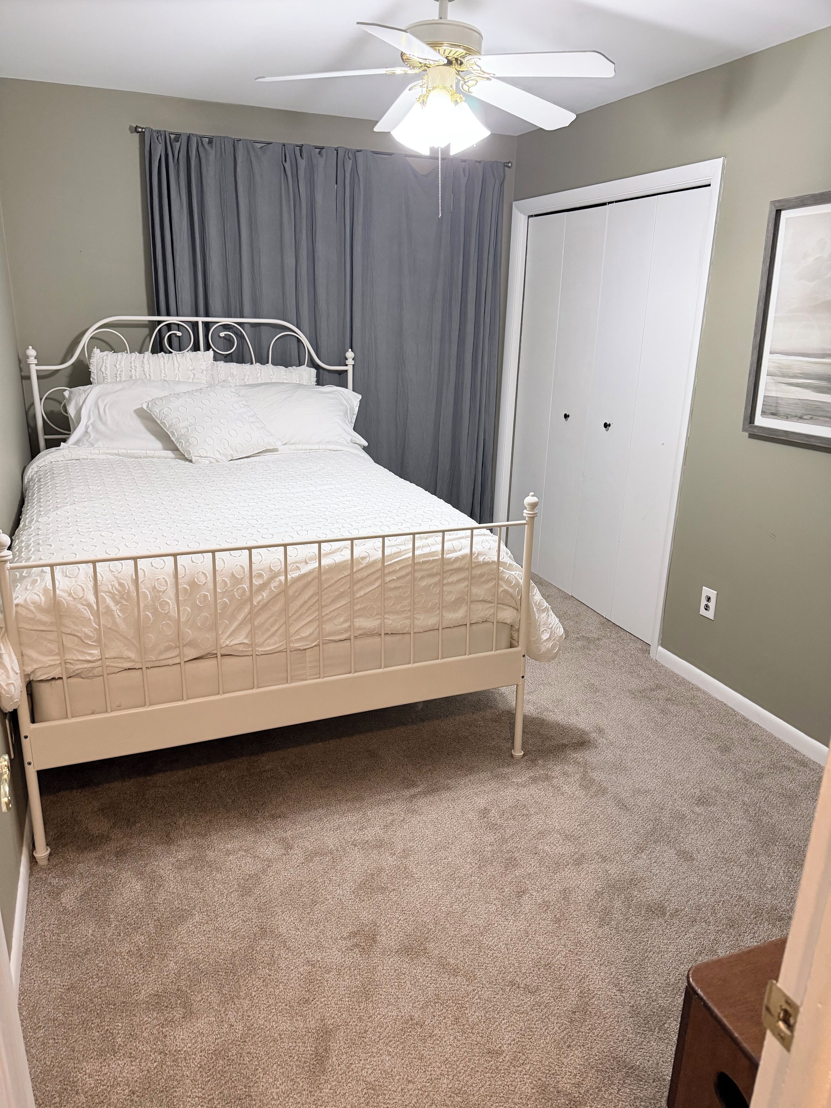 A bedroom with a bed, a ceiling fan, a door, and a carpeted floor.
