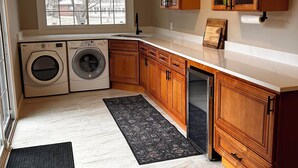 A kitchen with wooden cabinets, a ceiling fan, a window, a washing machine, and a countertop. - Spacious 3-bedroom house in beautiful Brighton. (Brighton)