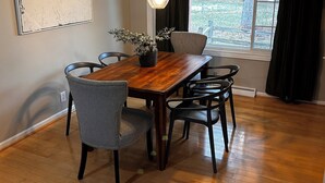 A dining area with a wooden table, grey upholstered chairs, and pendant lighting. - Spacious 3-bedroom house in beautiful Brighton. (Brighton)