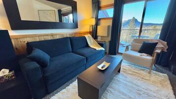 Une chambre d’hôtel moderne avec un canapé bleu foncé, une table basse en bois et un tapis à poils longs blanc.