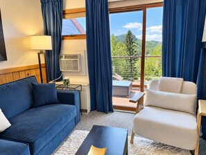 A room with a sofa, armchair, and a small table. There is a window with curtains, and a view of trees and mountains. - Lutsen Ski-In/Ski-Out | Moose Mtn Views | Jet Spa (Lutsen)