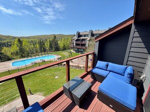 A balcony with a pool view, outdoor seating, and a wooden deck.