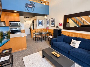 Ein modernes Wohnzimmer mit einem blauen Sofa, einem Couchtisch und einer Küchenzeile mit Mikrowelle und Herd.