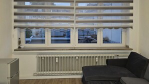A room with a radiator, a sofa, a small table, and a window with blinds.