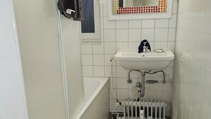 A small bathroom with a white sink, a mirror with a red frame, and a bathtub.