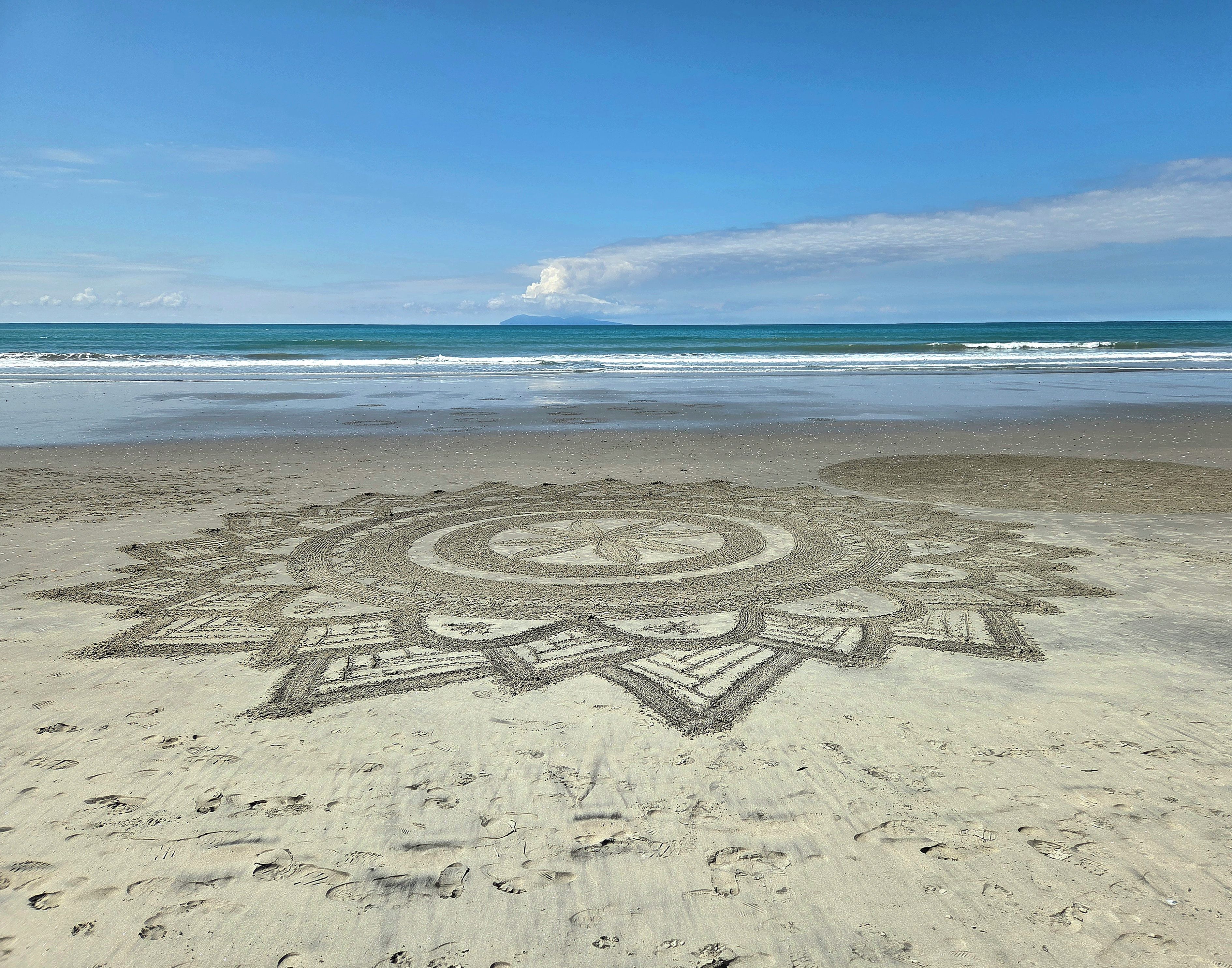 A beach with a large star-shaped sand drawing in the foreground.