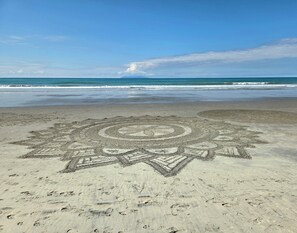 A beach with a large star-shaped sand drawing in the foreground. - Peace of Bali 1 bed cabin set in a tropical garden with WiFi & AC in Waihi Beach (Waihi Beach)