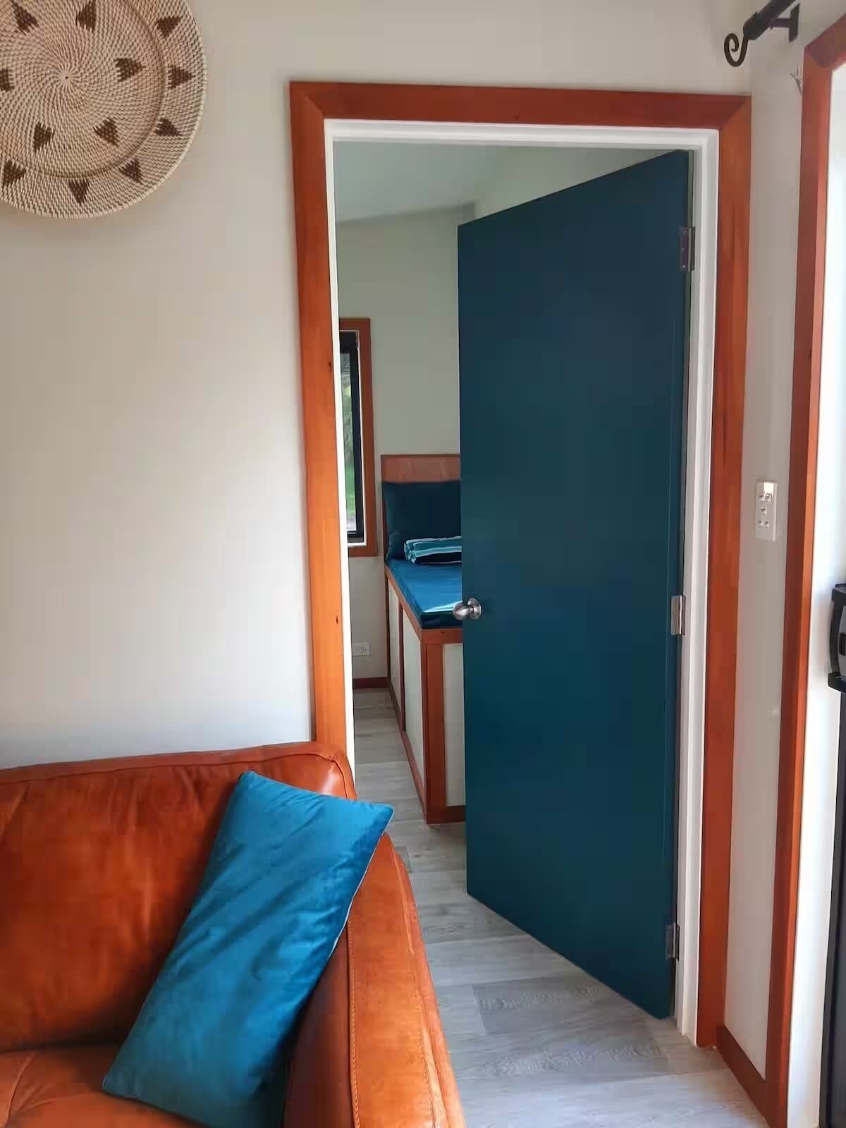 A room with a brown leather sofa, a blue pillow, a teal door, and a wooden floor.