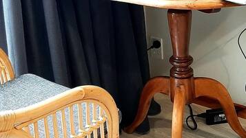Un portatile su un tavolo di legno con vista mare sullo schermo, una sedia in vimini e un quadro appeso al muro.