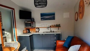 En kompakt opholdsstue med tekøkken, spiseplads og siddeområde med sofa og stole.