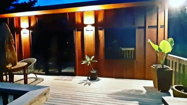 En træterrasse med gelænder, plantekasser og en bygning med oplyste vinduer.