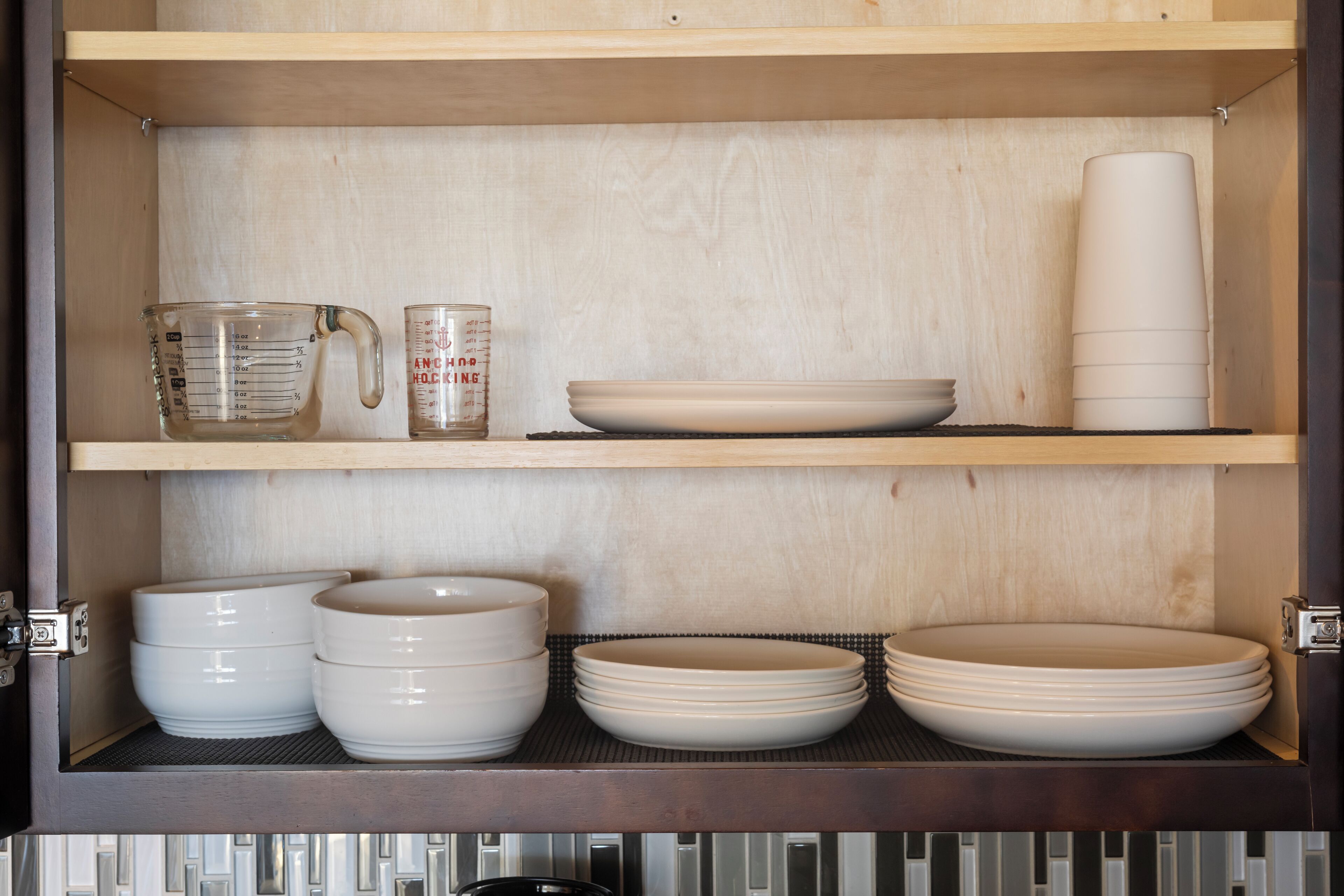 A kitchen cabinet with shelves holding various dishes and measuring cups.