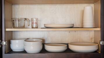 A kitchen cabinet with shelves holding various dishes and measuring cups.