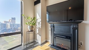 Ein modernes Wohnzimmer mit Kamin, einem großen Fenster und Stadtblick sowie einem flachbildfernseher, der darüber angebracht ist.