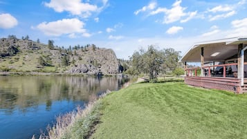 A lakeside property with a grassy lawn, a wooden deck, and a view of a rocky hill.