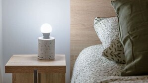 Una cama con ropa de cama estampada, cabecera de madera y mesita de noche con una lámpara de textura.