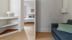 Un apartamento moderno con piso de madera, un sofá gris y un estante blanco.