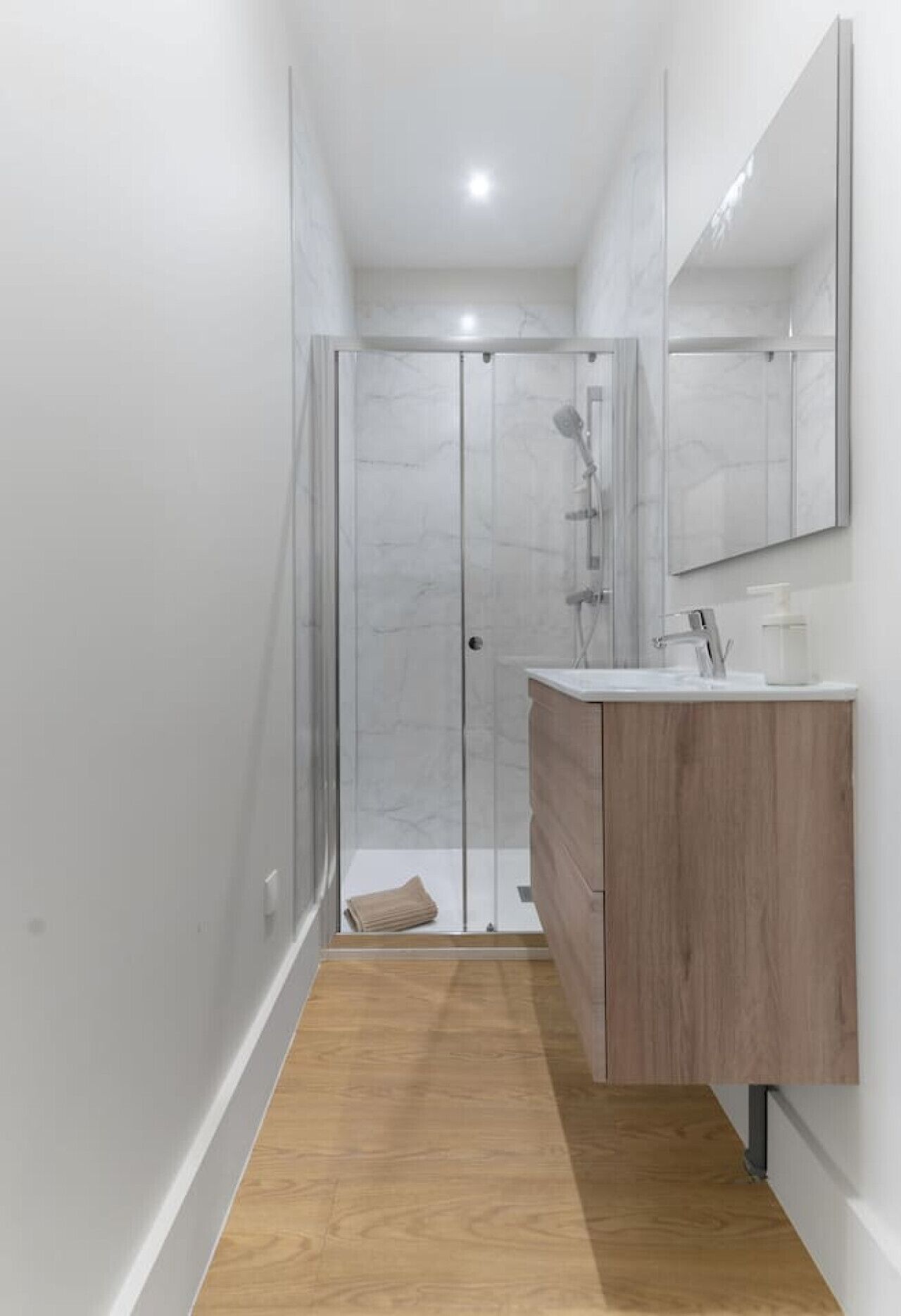 A modern bathroom with a glass shower enclosure, a wooden vanity, and a large mirror.