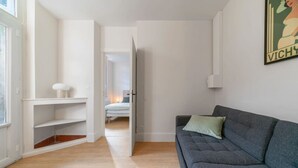 Una sala moderna con un sofá gris, un estante pequeño blanco y un acceso a otra habitación.