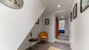 A narrow hallway with a wooden floor, a yellow chair, a small table with a book, and framed pictures on the walls. - Le Charlot - 27 rue charlot - Vichy (Vichy)