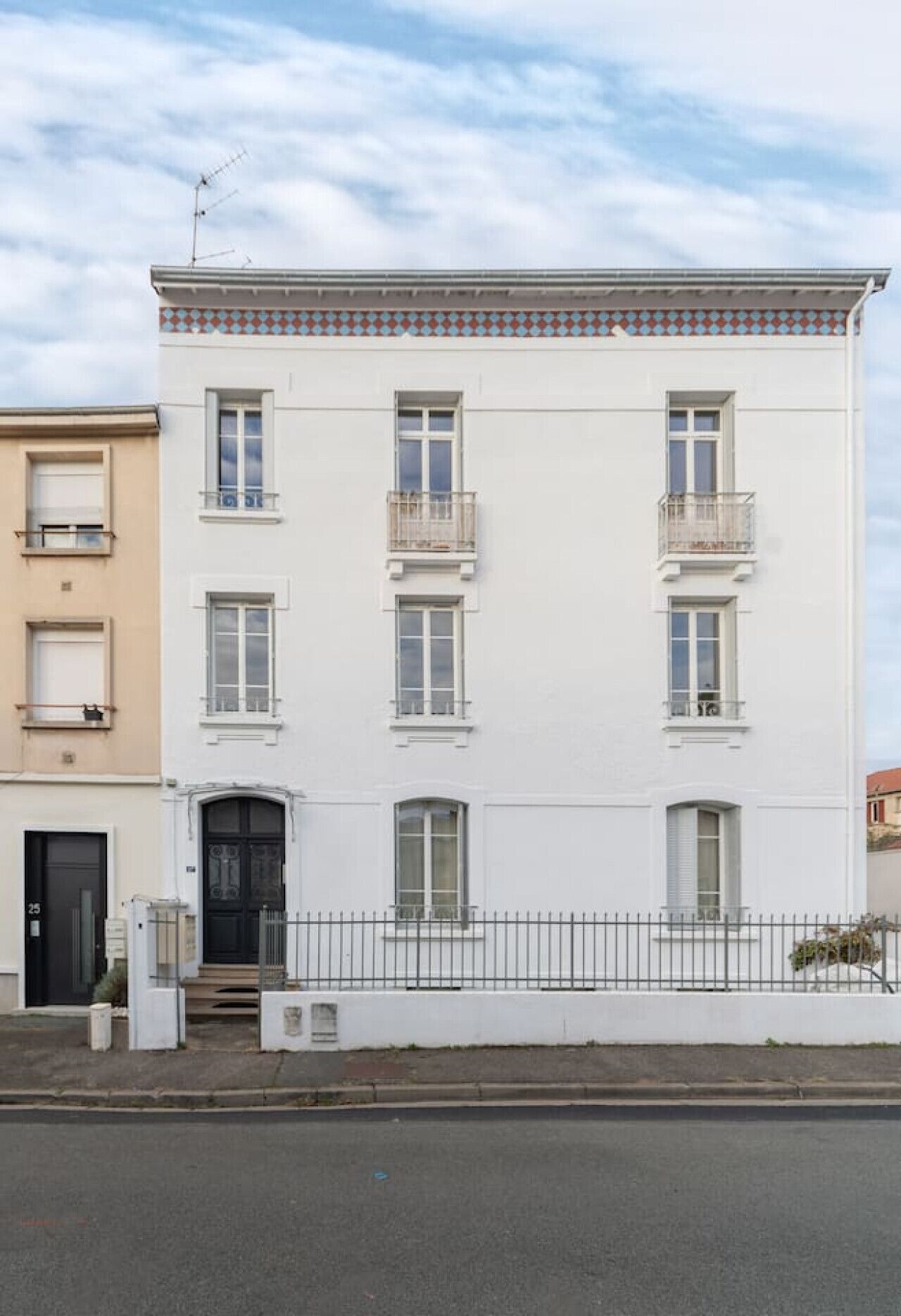 Un bâtiment blanc avec une porte noire, de nombreuses fenêtres et un balcon.