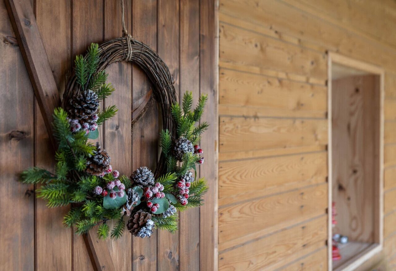 A wooden wall with a wreath made of pine cones, pine branches, and berries.