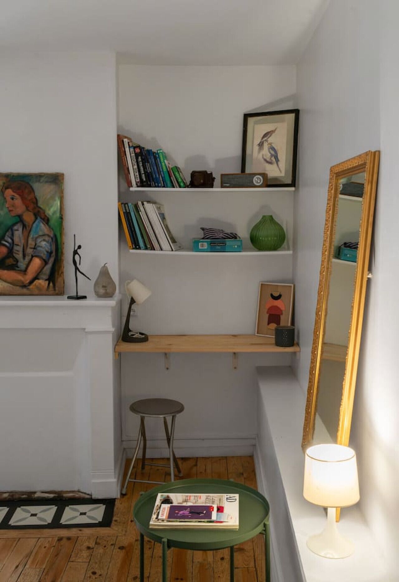 Una stanza piccola e stretta con una libreria, una scrivania, una sedia, uno specchio e una lampada.