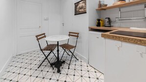 A compact kitchen with a round table and four chairs, a white door, and a tiled floor. - Le Paradis - 4 rue du Paradis - Clermont (Clermont-Ferrand)
