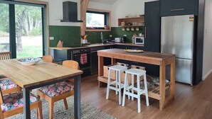 Moderni keittiö, jossa on puutasot, ruostumattomasta teräksestä valmistettu jääkaappi sekä ruokailutila, jossa on puinen pöytä ja tuolit.