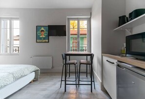 A compact room with a bed, a small table with two chairs, a TV mounted on the wall, and a kitchen area with a dishwasher and a microwave. - Le Desroziers 312 - 31 avenue Victoria - Vichy (Vichy)