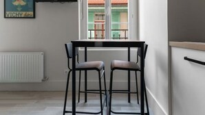 A modern kitchen with a dining table and two chairs, a window with a view of a building, and a mounted television. - Le Desroziers 312 - 31 avenue Victoria - Vichy (Vichy)