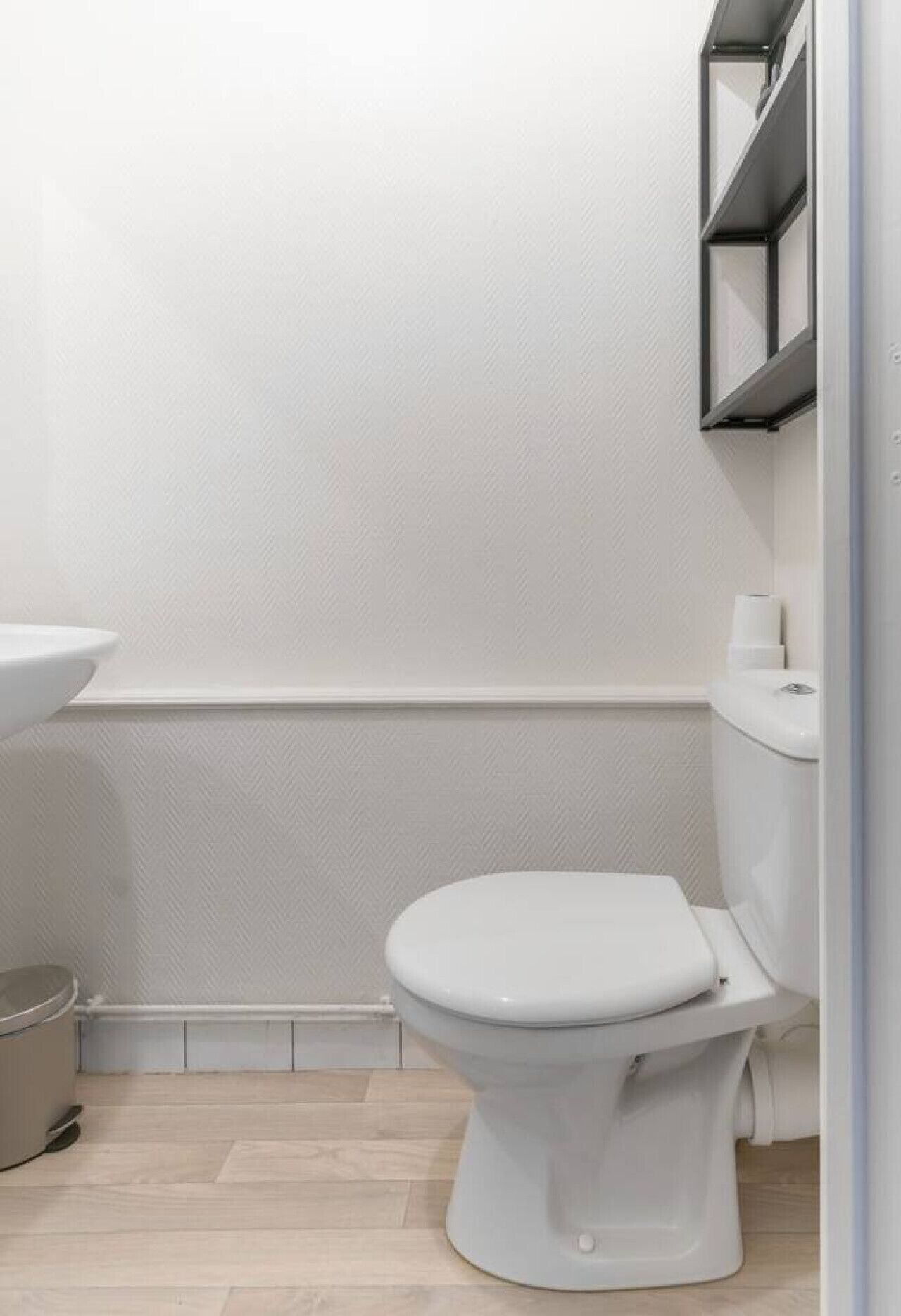 Een compacte, moderne badkamer met een wit toilet, een witte wastafel en een toiletrolhouder aan de muur.