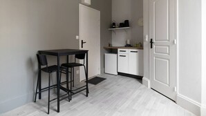 Cozinha compacta com área de refeições, armários brancos, uma geladeira pequena e uma porta branca.