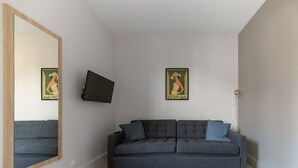 Uma sala de estar moderna com um sofá cinzento, duas almofadas, uma televisão de tela plana na parede e dois cartazes.