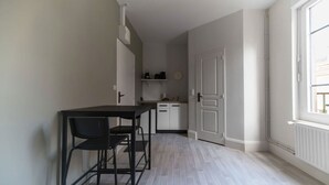 Cozinha pequena e luminosa com mesa e cadeiras, porta branca e janela que permite entrada de luz natural.
