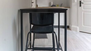 Um corredor estreito com uma mesa e cadeira de metal preto, uma porta branca e uma estante com utensílios de cozinha.