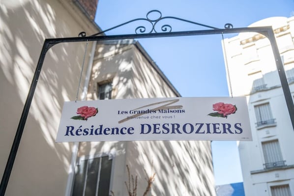 Un letrero que dice 'Résidence DESROZIERS', con un mensaje de bienvenida y dos rosas rosadas.