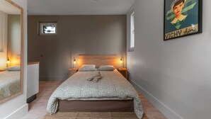 A modern bedroom with a large bed, bedside lamps, a small window, and a poster on the wall.