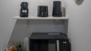 A small kitchenette with a microwave, toaster, and coffee maker on a shelf, a clock on the wall, and a hanging light fixture.