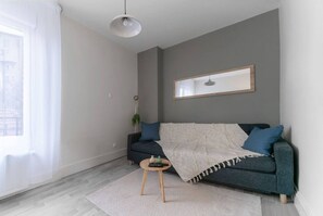 A modern living room with a grey sofa, a round wooden coffee table, and a large window with sheer curtains. - Le Desroziers 321 - 31 avenue Victoria - Vichy (Vichy)