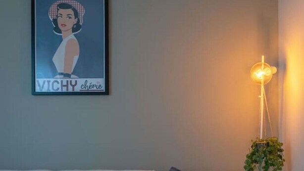 Una sala moderna con un sofá oscuro, una manta blanca y un cartel enmarcado en la pared.