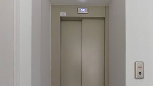 Un pasillo estrecho con piso alfombrado que conduce a una puerta cerrada de ascensor.
