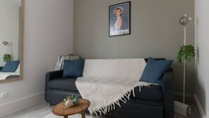 Una sala de estar moderna con un sofá gris oscuro, una manta blanca y una pequeña mesita de madera con un adorno de piña.