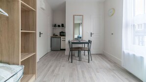 A compact room with a wooden wardrobe, a small kitchenette, a dining table with chairs, and a large mirror.